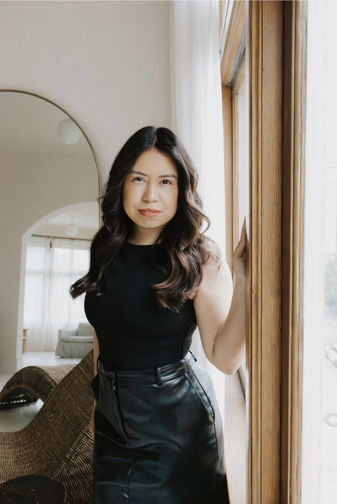 Rebeca, hairstylist, standing by a window in a bright room